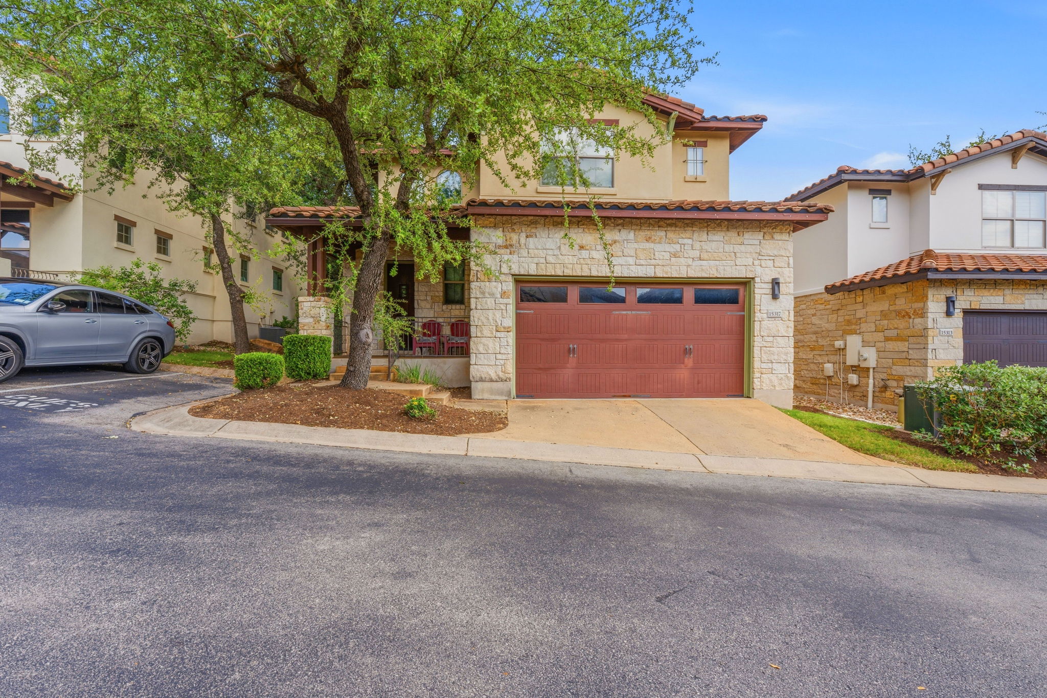 15317 Falconhead Grove Loop Austin, TX 78738 - Photo 6 of 36 Mediterranean-style residence featuring a terracotta tile roof, stone facade accents, an attached garage, a covered entry porch, and mature trees