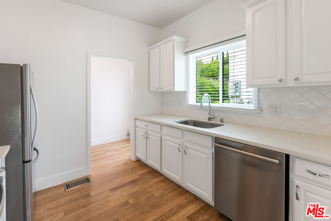 1253 South Rimpau Boulevard Los Angeles, CA 90019 - Photo 53 of 71 a kitchen with stainless steel appliances granite countertop a sink a window and wooden floor