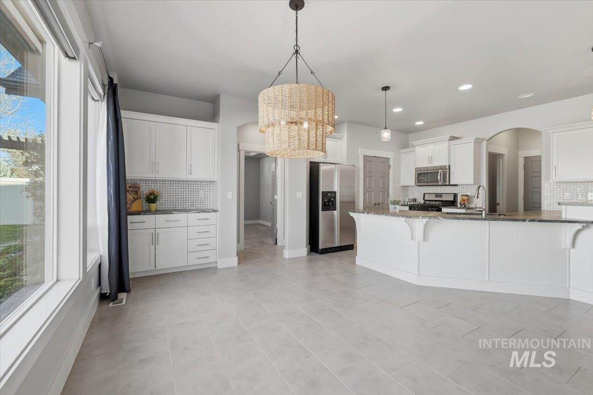 15381 Silver Oak Way Caldwell, ID 83607 - Photo 12 of 48 Kitchen featuring arched walkways, stainless steel appliances, white cabinetry, a breakfast bar, and backsplash