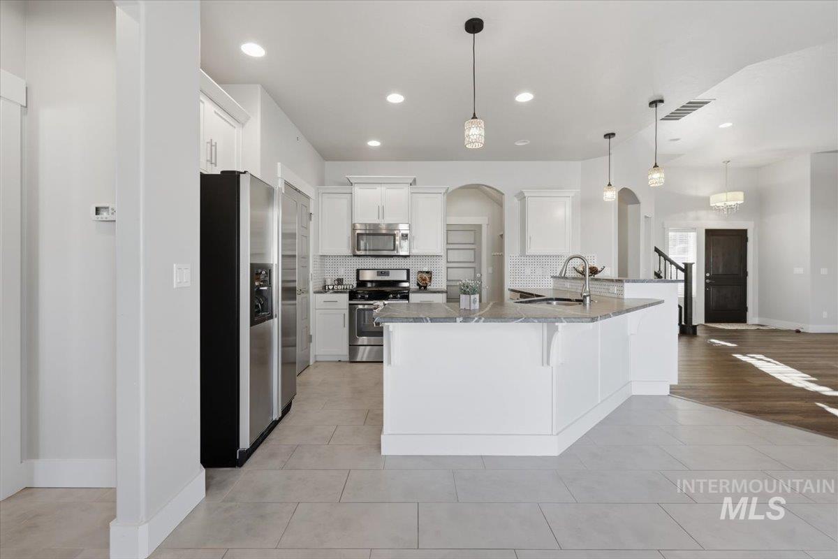 15381 Silver Oak Way Caldwell, ID 83607 - Photo 16 of 48 Kitchen with arched walkways, a kitchen bar, stainless steel appliances, white cabinetry, and dark stone counters