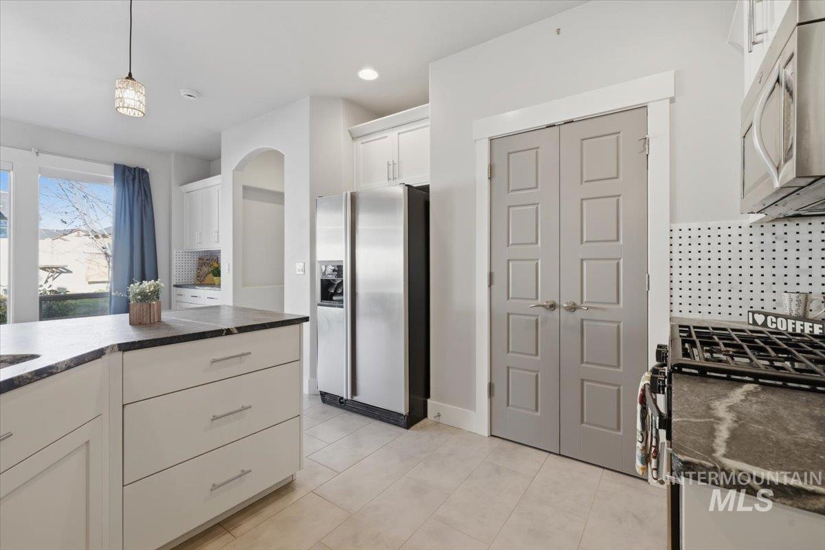 15381 Silver Oak Way Caldwell, ID 83607 - Photo 19 of 48 Kitchen featuring backsplash, stainless steel appliances, dark countertops, white cabinets, and decorative light fixtures