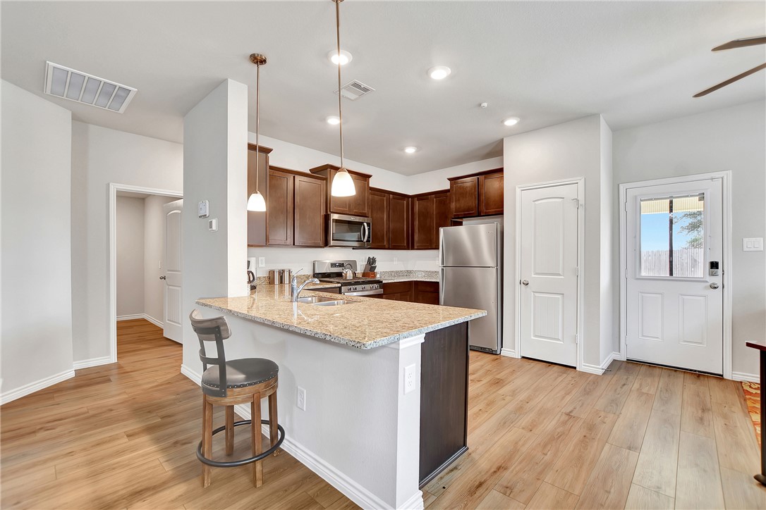 909 Davy Street Brenham, TX 77833 - Photo 12 of 35 Kitchen featuring stainless steel appliances, a peninsula, dark wood finish cabinetry, light stone counters, and a kitchen bar