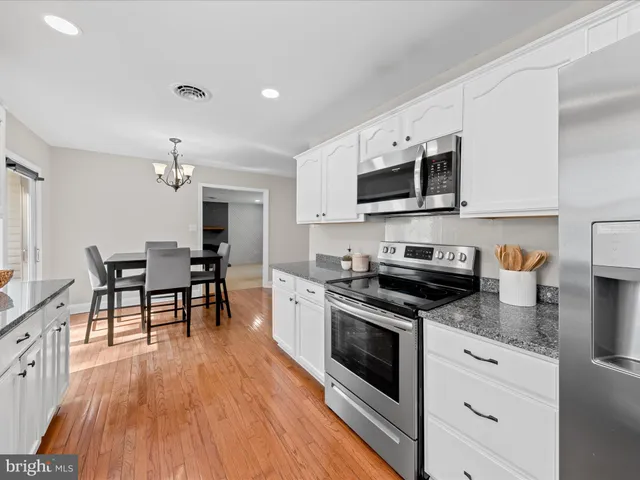 a kitchen with stainless steel appliances granite countertop a stove top oven a sink dishwasher a dining table and chairs with wooden floor