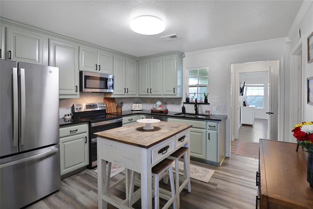 271 East Houston Street Van Alstyne, TX 75495 - Photo 12 of 40 a kitchen with kitchen island granite countertop a sink stove a refrigerator and white cabinets with wooden floor