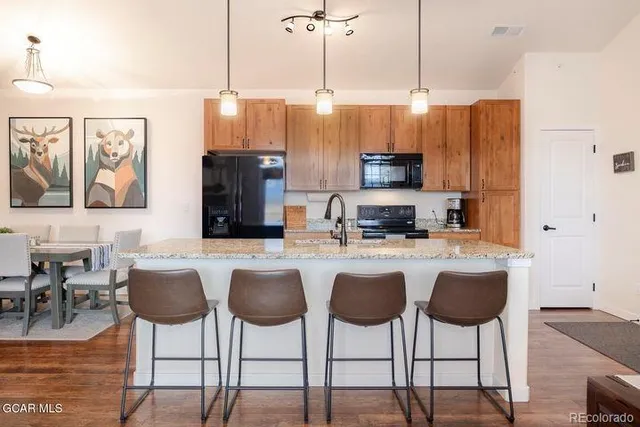 a kitchen with stainless steel appliances granite countertop a stove a sink a refrigerator a dining table and chairs with wooden floor