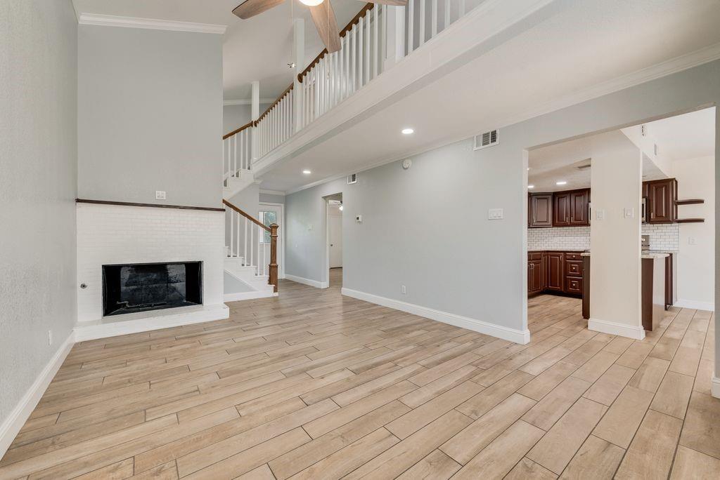 219 West Rochelle Road Irving, TX 75062 - Photo 5 of 29 Spacious living area featuring wood-finish flooring, a white brick fireplace, and a two-story ceiling with an upper-level balcony overlooking the space
