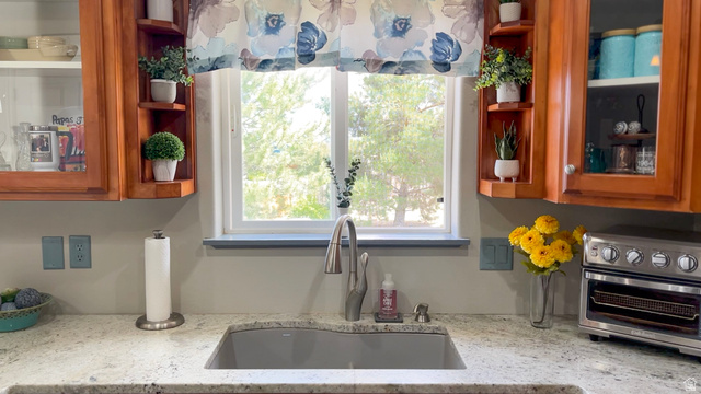 1797 Sunset Road Enoch, UT 84721 - Photo 15 of 80 Kitchen area featuring a light-colored countertop, an undermount sink with a gooseneck faucet, light wood-finish cabinetry with glass-front doors, and a double-pane window