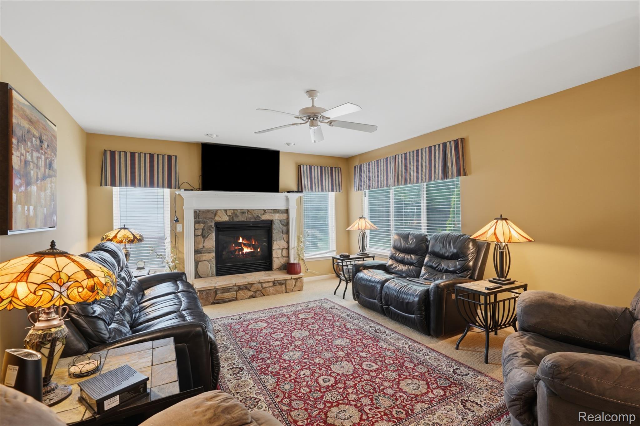 170 Fairhill Way Howell, MI 48843 - Photo 18 of 46 Living area featuring a stone fireplace with a white mantel, neutral carpeting, and multiple windows with blinds