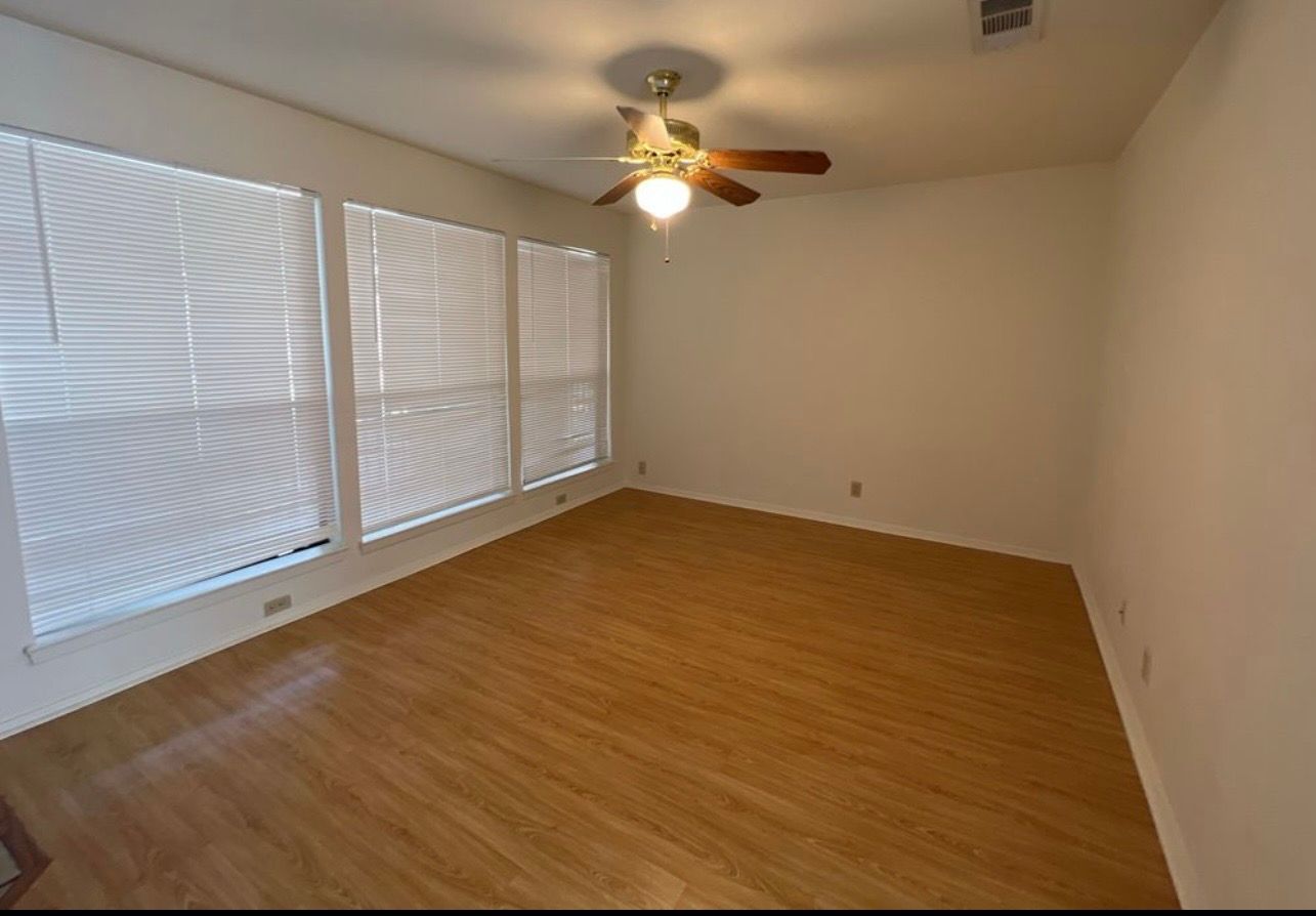 3115 Helms Street, Unit 111 Austin, TX 78705 - Photo 9 of 13 Blinds adorn multiple windows, illuminating a spacious room with warm wood flooring.