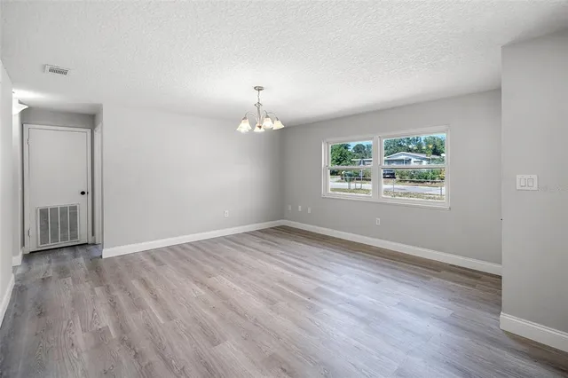 an empty room with wooden floor chandelier and windows