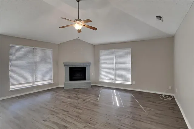 a view of an empty room with wooden floor fireplace and a window