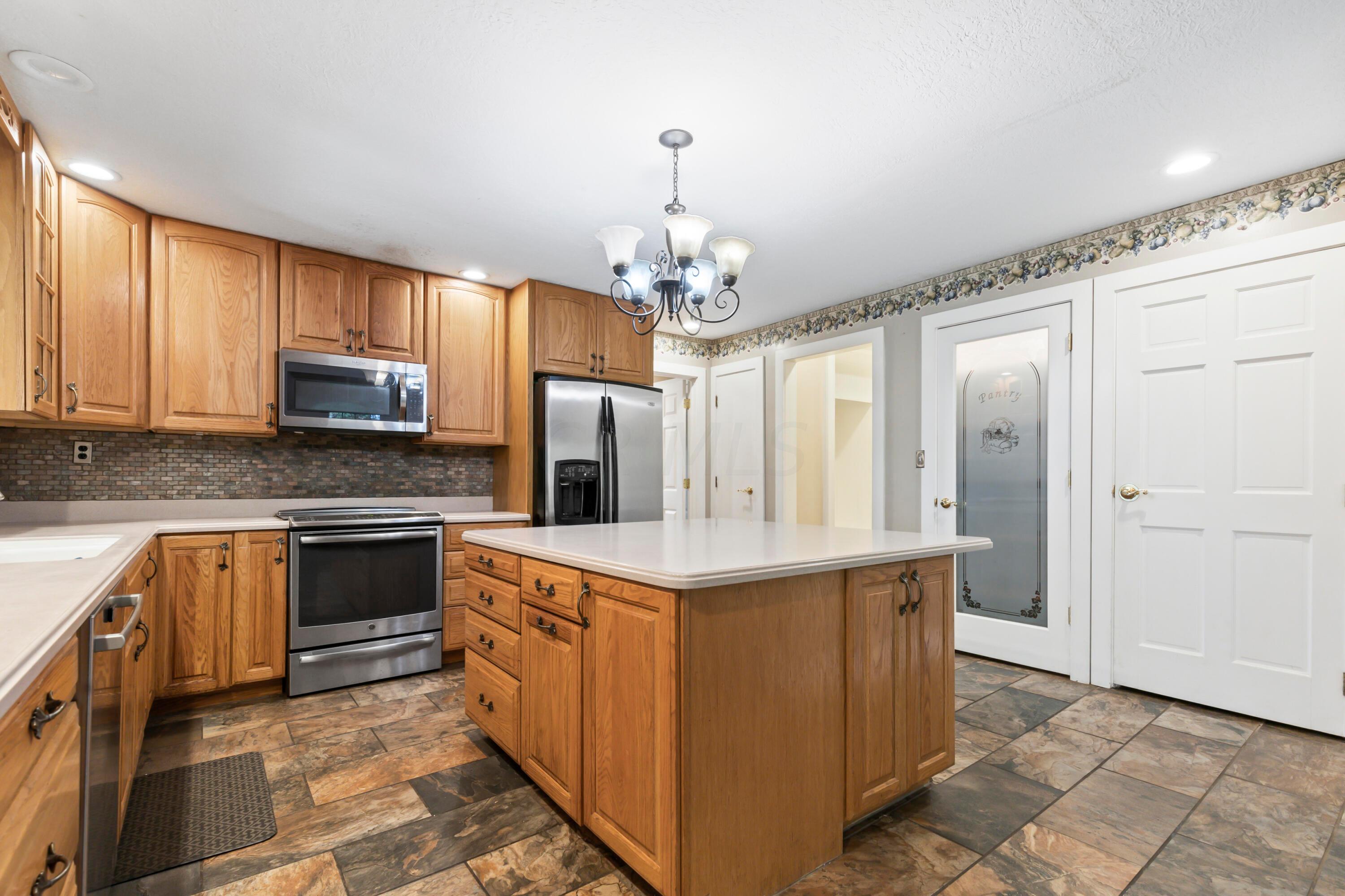 9495 Kilbourne Road Sunbury, OH 43074 - Photo 16 of 84 • Completely updated ~2003
• New slate flooring ~2014
• Tan painted walls
• Corian countertops
• 5’ x 5’ center island with
breakfast bar ledge
• 42” oak, raised panel cabinets
• New Bosch® dishwasher
~10/2014
• Extra deep, double bowl sink
with sprayer
• New Frigidaire® microwave
~2013
• New General Electric® electric
range ~2015
• New Whirlpool® refrigerator
~2012/2013
• Slate tile backsplash
• Insinkerator® disposal
• Can lighting
• Hanging light
• Pantry with glass front door
• Second pantry