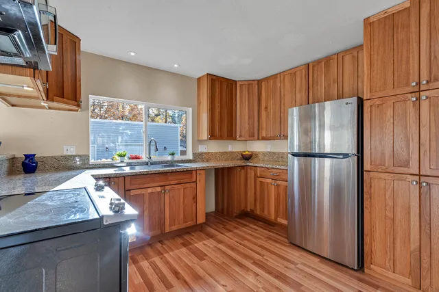 a kitchen with stainless steel appliances granite countertop a refrigerator a sink dishwasher and wooden cabinets with wooden floor