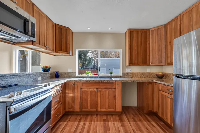 a kitchen with stainless steel appliances a sink dishwasher a stove top oven a refrigerator with wooden floor and cabinets