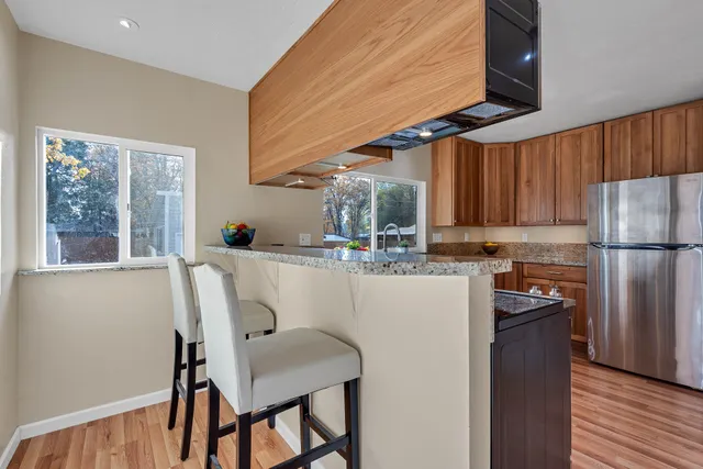 a kitchen with stainless steel appliances granite countertop a refrigerator a sink dishwasher a stove a dining table and chairs with wooden floor