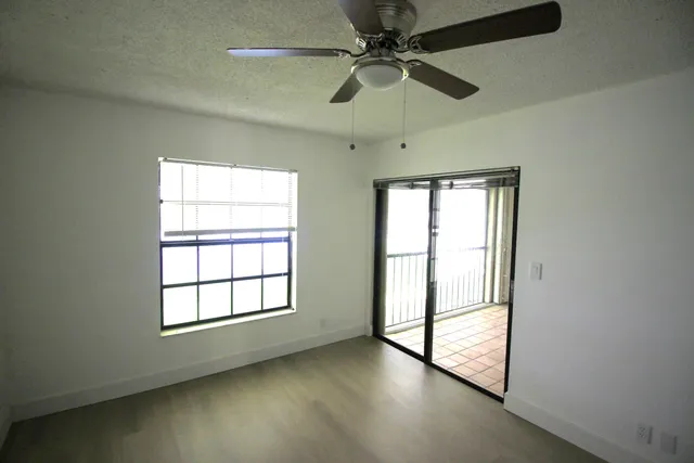 an empty room with wooden floor fan and windows