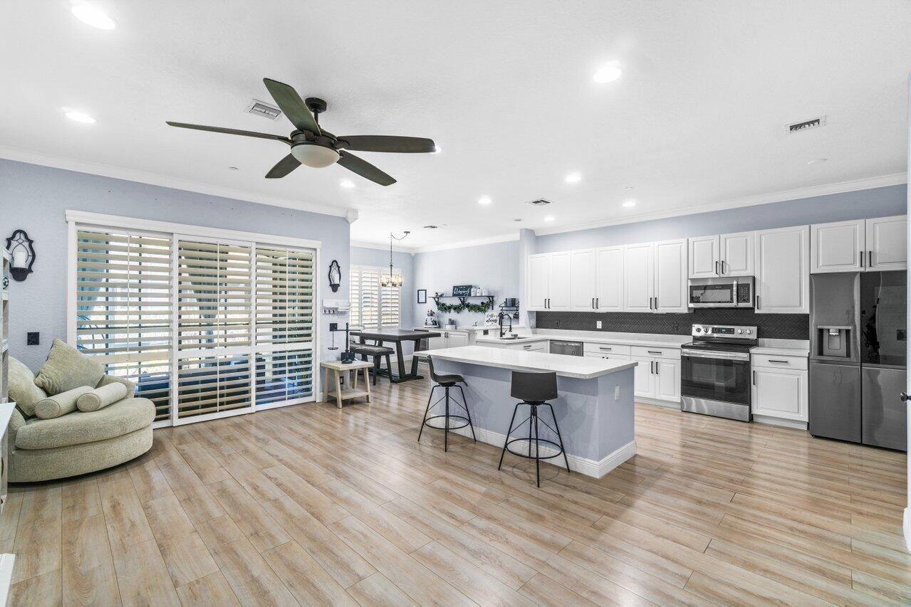 a living room with stainless steel appliances kitchen island granite countertop a stove a refrigerator a dining table and chairs with wooden floor