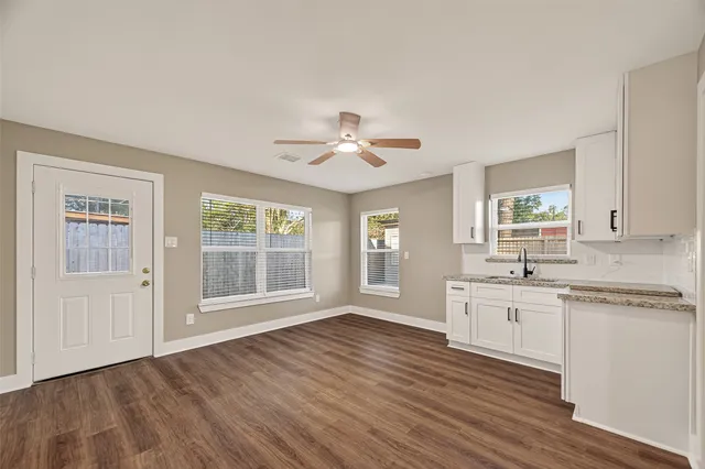 a large kitchen with granite countertop a stove a sink white cabinets and wooden floor next to a window