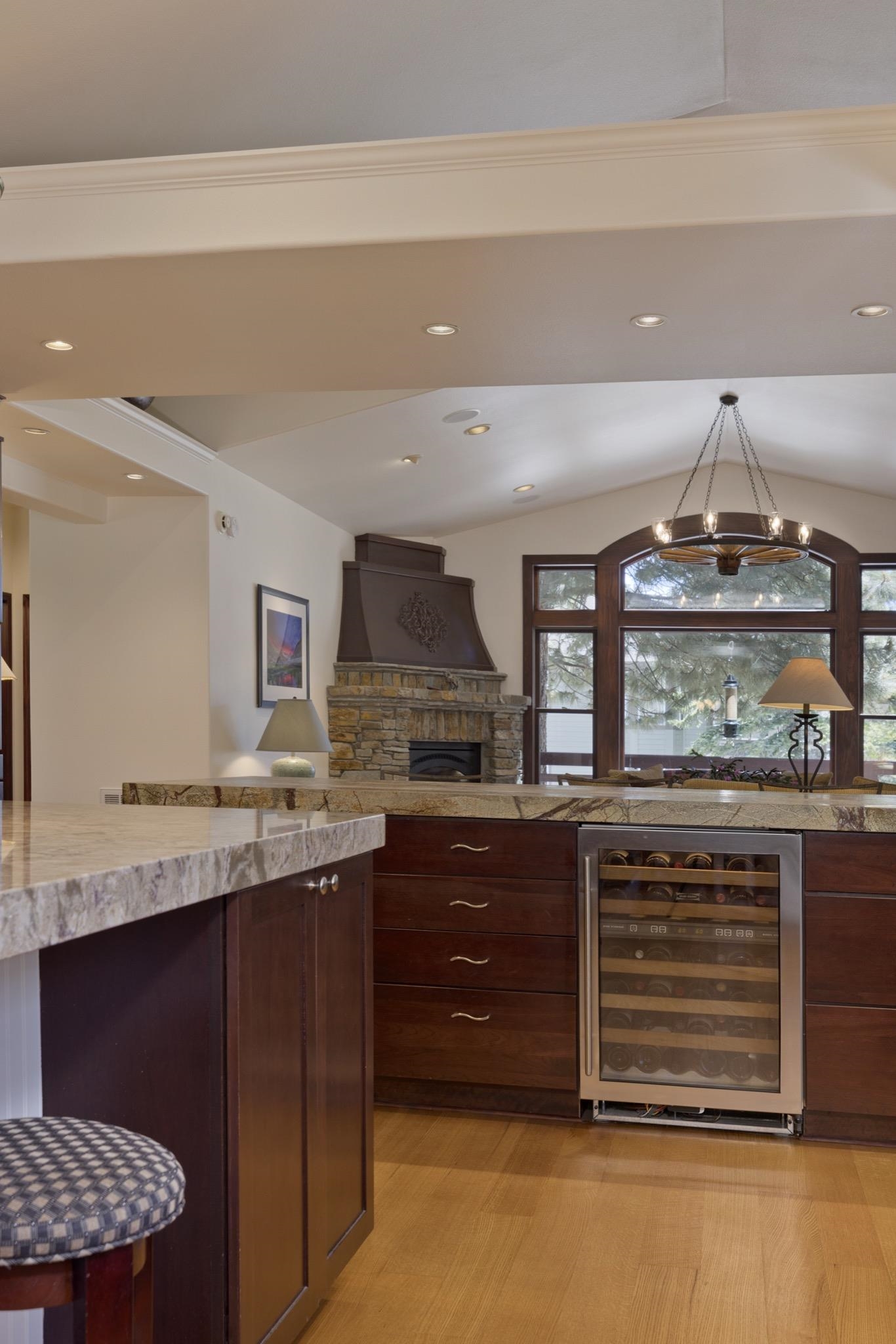 378 Ridge Way Mammoth Lakes, CA 93546 - Photo 16 of 43 Integrated kitchen and living area featuring granite countertops, wood-finish flooring, a stainless steel beverage refrigerator, dark wood cabinetry, and a stone fireplace with a decorative mantel and a large arched window