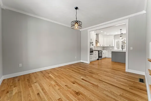 a view of empty room with wooden floor and kitchen view