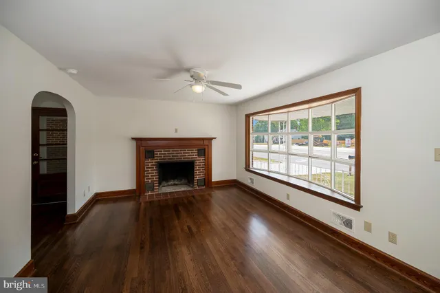 a view of an empty room with wooden floor fireplace and a window