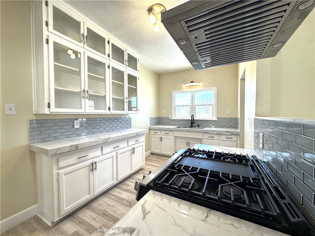 13407 Holly Street Trona, CA 93562 - Photo 15 of 25 Kitchen – 13407 Holly
Bright and modern kitchen with white shaker cabinets, glass-front uppers, and abundant storage.
Striking subway tile backsplash and marble-look counters add timeless style.
Stainless steel gas range with sleek hood vent creates a functional and eye-catching focal point.
Large dual windows above the sink bring in natural light and showcase desert views.
Open, efficient layout makes this kitchen both stylish and practical for everyday living.