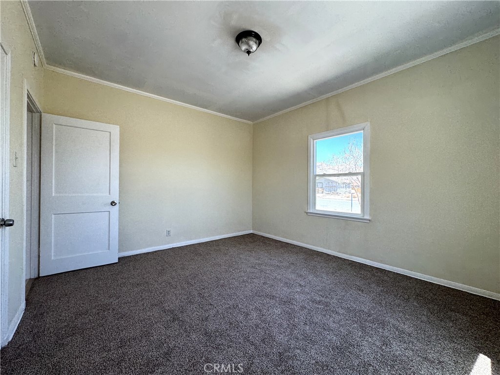 13407 Holly Street Trona, CA 93562 - Photo 17 of 25 comfortable bedroom with brand-new carpet and neutral wall tones, offering a fresh, move-in ready feel. Two windows provide natural light and ventilation, creating a bright and welcoming space. Spacious layout works perfectly as a guest room, secondary bedroom, or office. Simple design makes it easy to furnish and style to fit your needs.