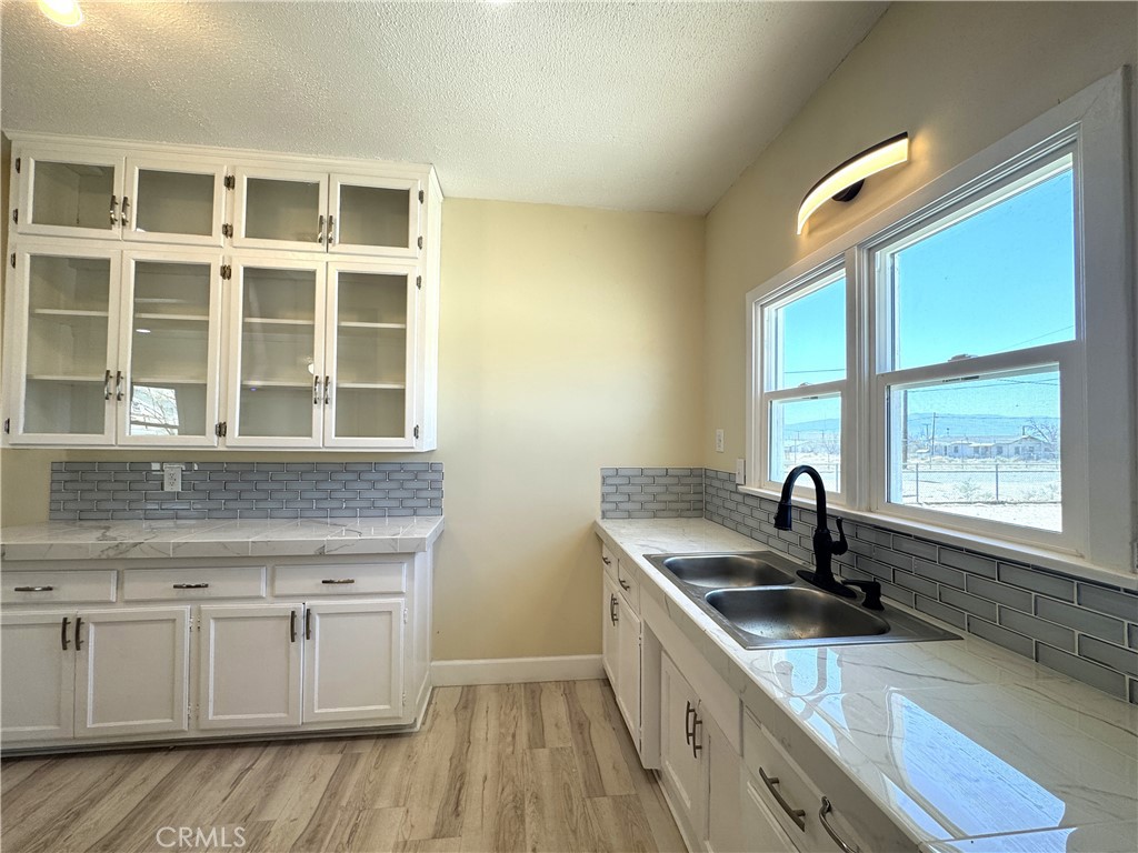 13407 Holly Street Trona, CA 93562 - Photo 5 of 25 (Sink + Counter Space + Cabinetry)
Bright double window above the sink brings in natural light while framing backyard views.
Expansive counters with a marble-look finish provide plenty of prep space.
Crisp subway tile backsplash blends classic style with modern appeal.
White cabinetry with brushed hardware offers generous storage and a timeless look