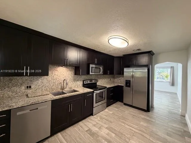 a kitchen with stainless steel appliances granite countertop a sink a stove a refrigerator cabinets and a counter top space