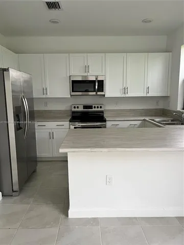 a kitchen with stainless steel appliances granite countertop a refrigerator a stove a sink and white cabinets