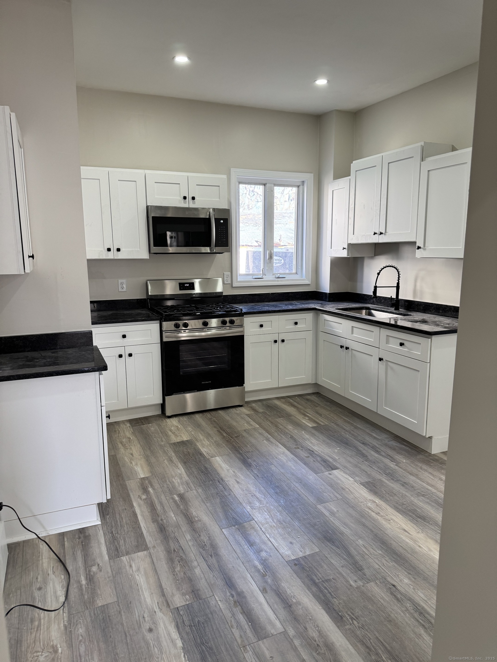 a large kitchen with stainless steel appliances granite countertop a stove a sink white cabinets and a wooden floor