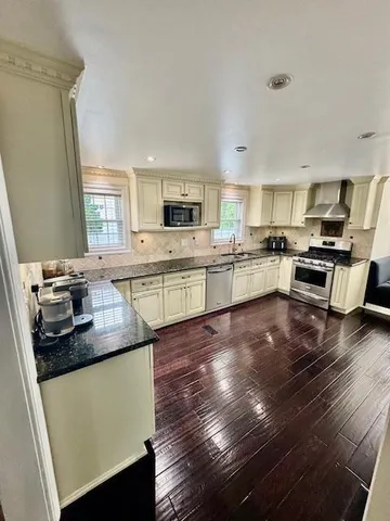 a kitchen with kitchen island granite countertop a sink dishwasher stove top oven and cabinets with wooden floor