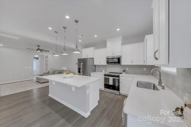 a large white kitchen with a stove a sink a refrigerator and a dining table with wooden floor