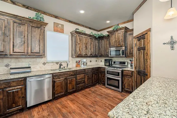 a kitchen with stainless steel appliances granite countertop a stove top oven a sink dishwasher and a refrigerator with wooden floor