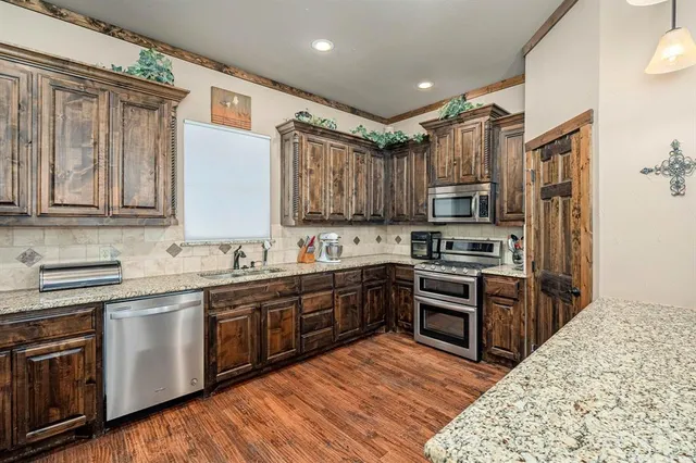 a kitchen with stainless steel appliances granite countertop a stove top oven a sink dishwasher and a refrigerator with wooden floor