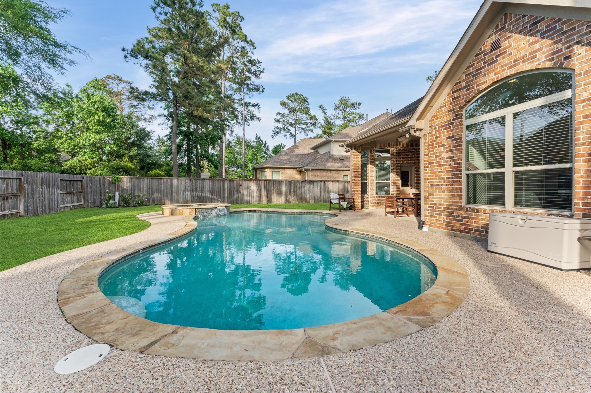 70 Valera Ridge Drive Spring, TX 77389 - Photo 7 of 37 This photo showcases a beautiful backyard with a kidney-shaped pool surrounded by a stone patio, lush green lawn, and a brick house. Tall trees provide natural privacy and shade, creating a serene outdoor retreat.