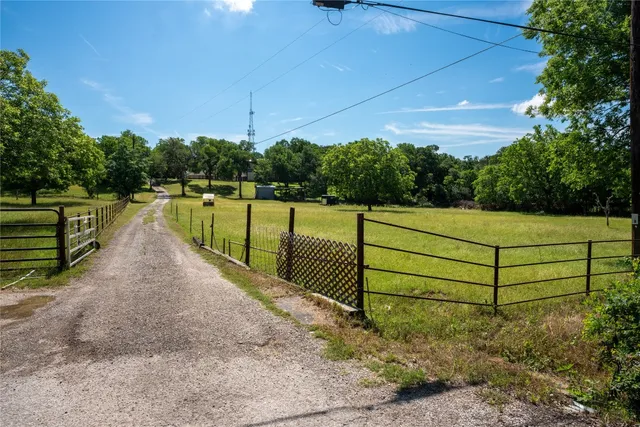 a view of a street with a yard and large trees