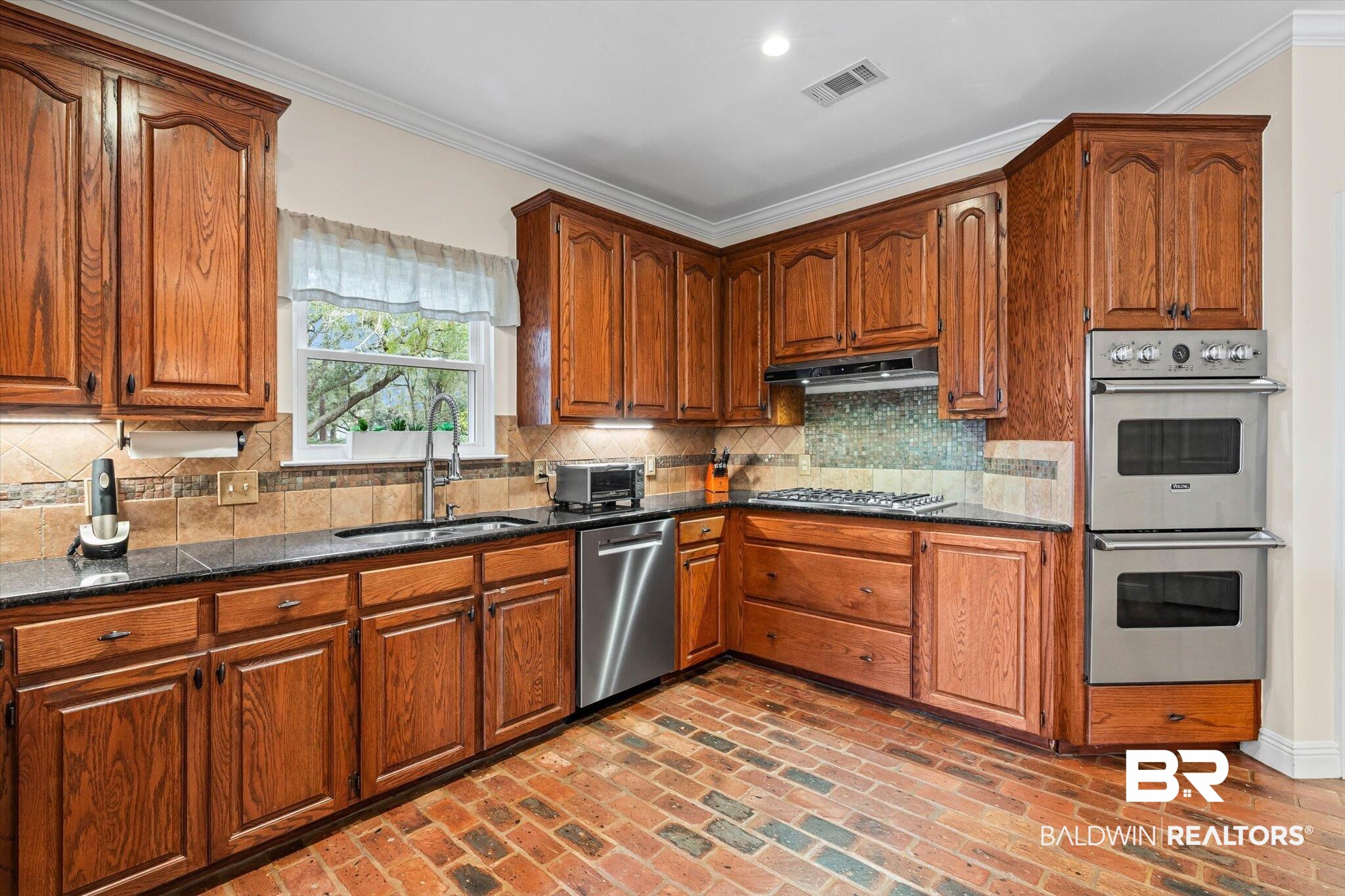 4851 Audubon Drive Mobile, AL 36619 - Photo 10 of 46 Kitchen featuring appliances with stainless steel finishes, brown cabinetry, brick flooring, dark stone counters, and ornamental molding