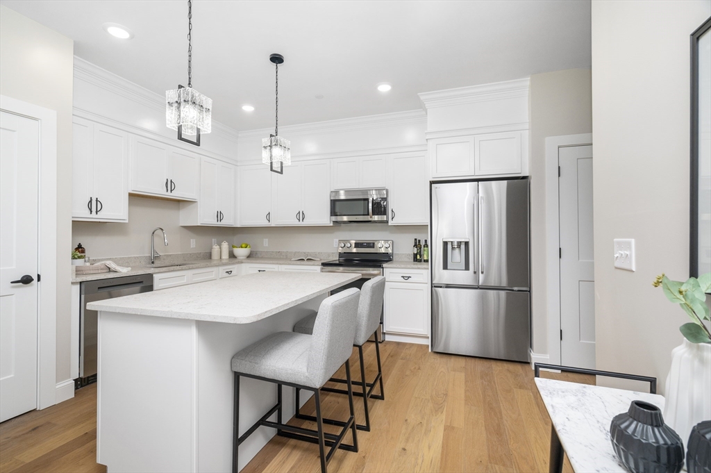 36 Old Louisquisset Pike, Unit 106 North Smithfield, RI 02896 - Photo 9 of 30 a kitchen with kitchen island a refrigerator a stove a sink and a refrigerator with wooden floor