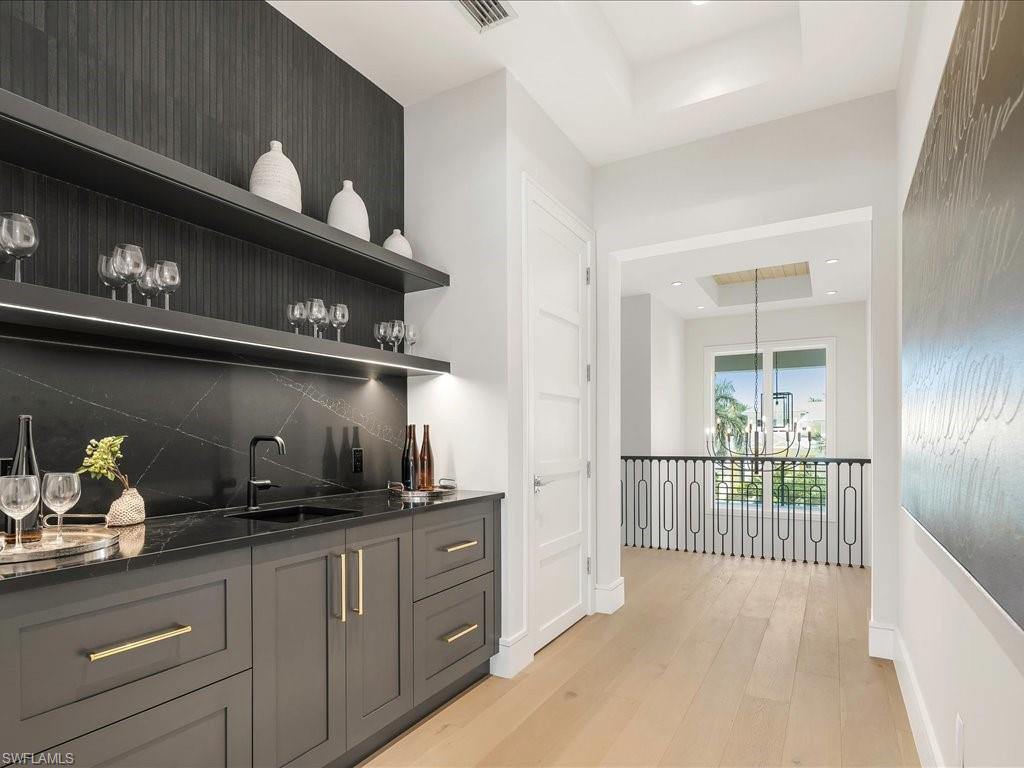 612 Binnacle Drive Naples, FL 34103 - Photo 41 of 50 Bar featuring a tray ceiling, wet bar, decorative backsplash, a sink, and light wood-style floors