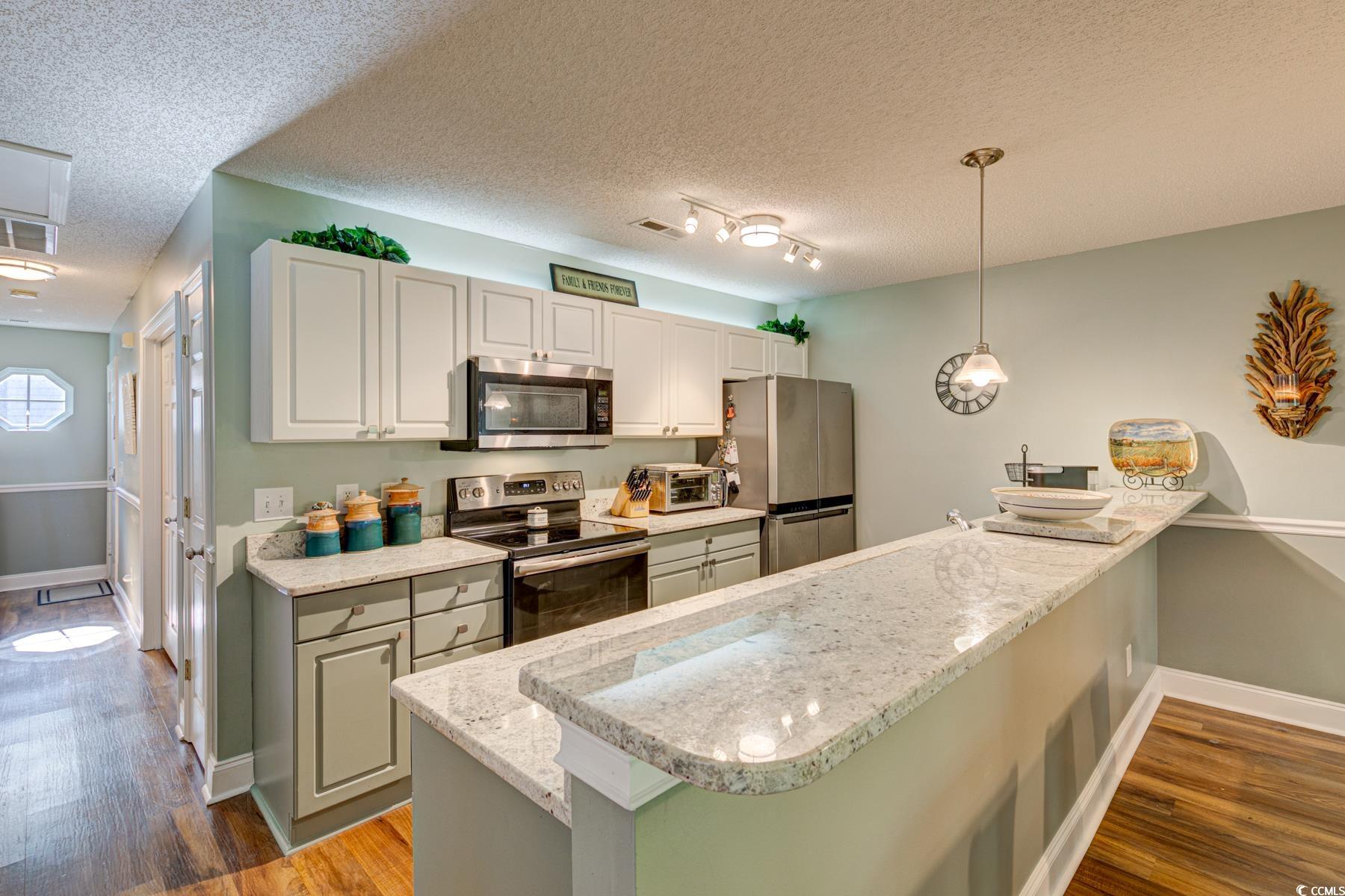 4840 Moss Creek Loop, Unit 36 Murrells Inlet, SC 29576 - Photo 13 of 37 Kitchen with stainless steel appliances, dark wood-style flooring, light stone countertops, a textured ceiling, and decorative light fixtures