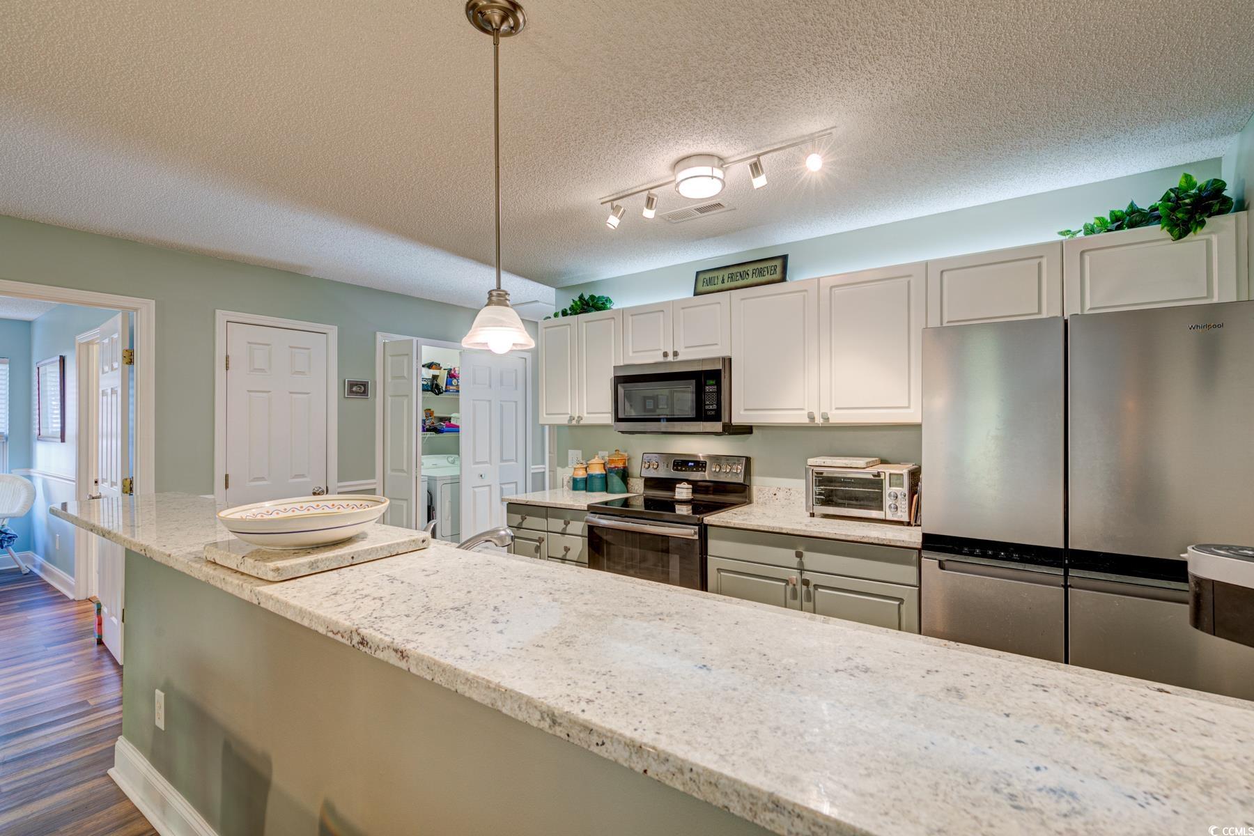 4840 Moss Creek Loop, Unit 36 Murrells Inlet, SC 29576 - Photo 14 of 37 Kitchen featuring stainless steel appliances, a textured ceiling, light stone counters, hanging light fixtures, and dark wood-style flooring