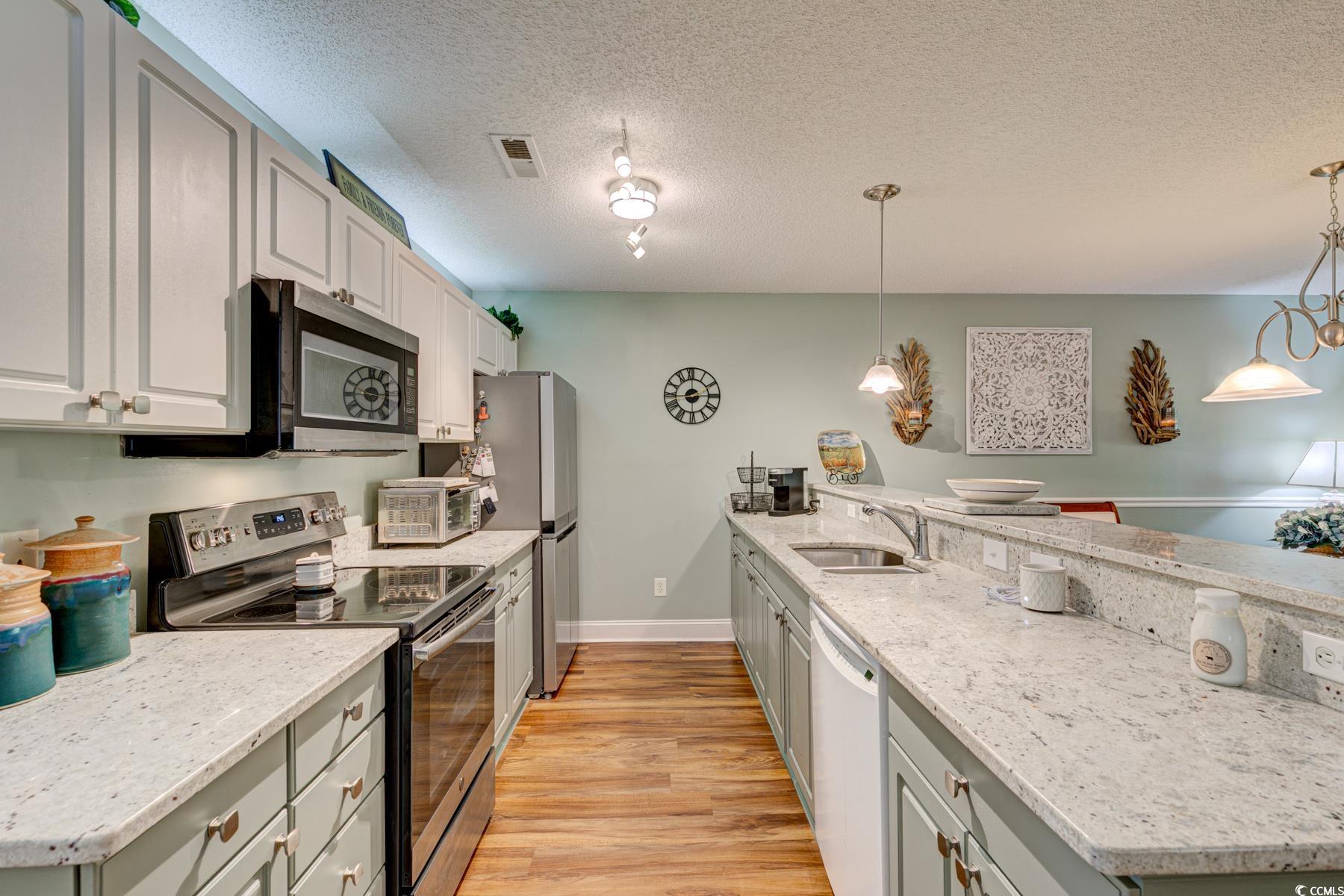 4840 Moss Creek Loop, Unit 36 Murrells Inlet, SC 29576 - Photo 15 of 37 Kitchen with appliances with stainless steel finishes, a peninsula, light stone countertops, a textured ceiling, and light wood-style flooring