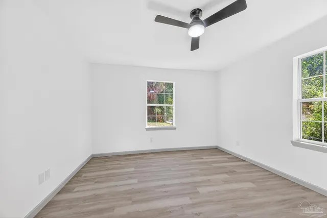 an empty room with wooden floor ceiling fan and windows