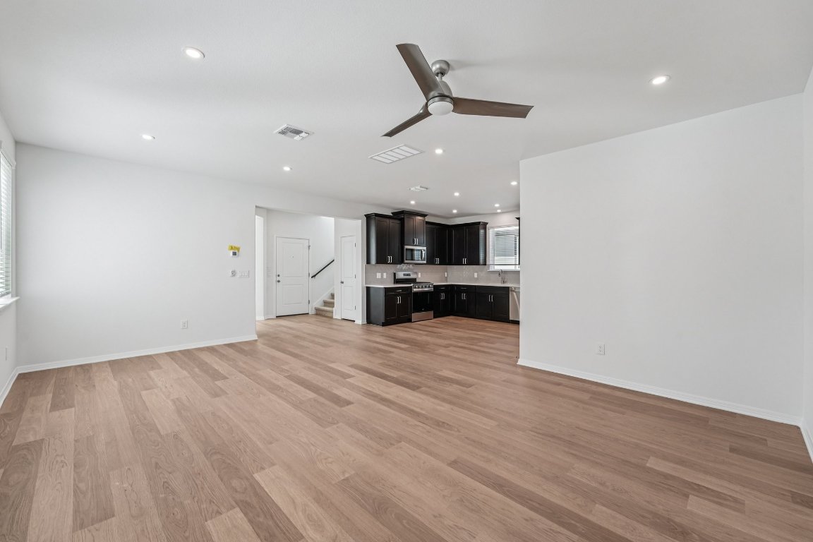 6309 Marsh Lane Buda, TX 78610 - Photo 2 of 39 an empty room with wooden floor ceiling fan and kitchen view