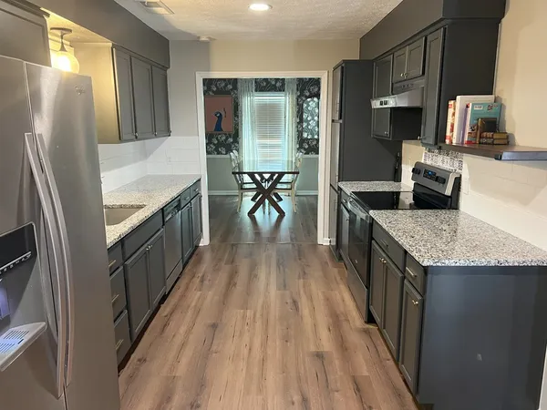 a kitchen with granite countertop a refrigerator a stove top oven a sink and dishwasher