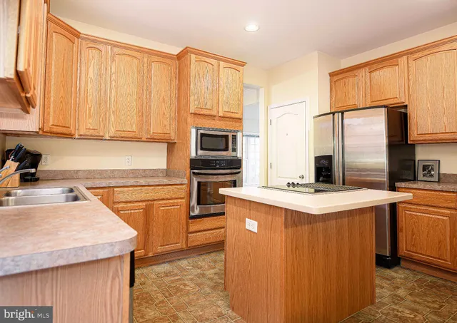 a kitchen with stainless steel appliances granite countertop a stove top oven a sink dishwasher and a refrigerator with wooden cabinets