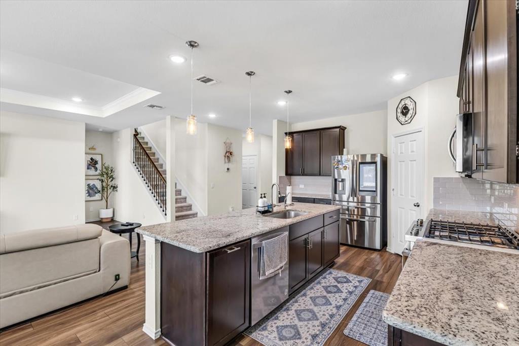 1201 Timberhurst Trail Fort Worth, TX 76131 - Photo 11 of 40 Open-concept kitchen featuring granite countertops, dark wood-finish cabinetry, stainless steel appliances, and a central island with an integrated sink