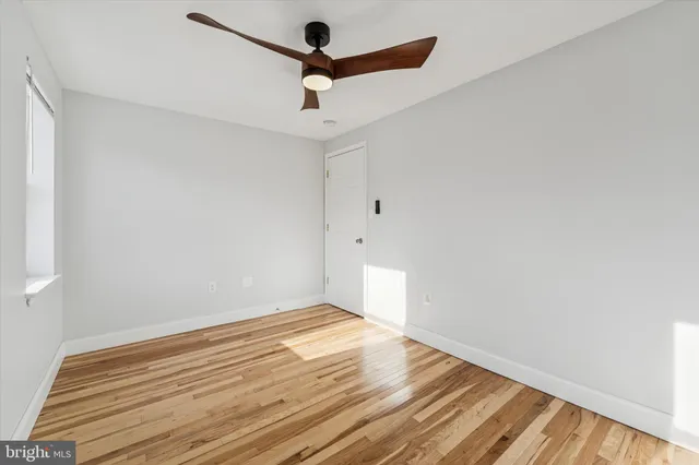 an empty room with wooden floor ceiling fan and window