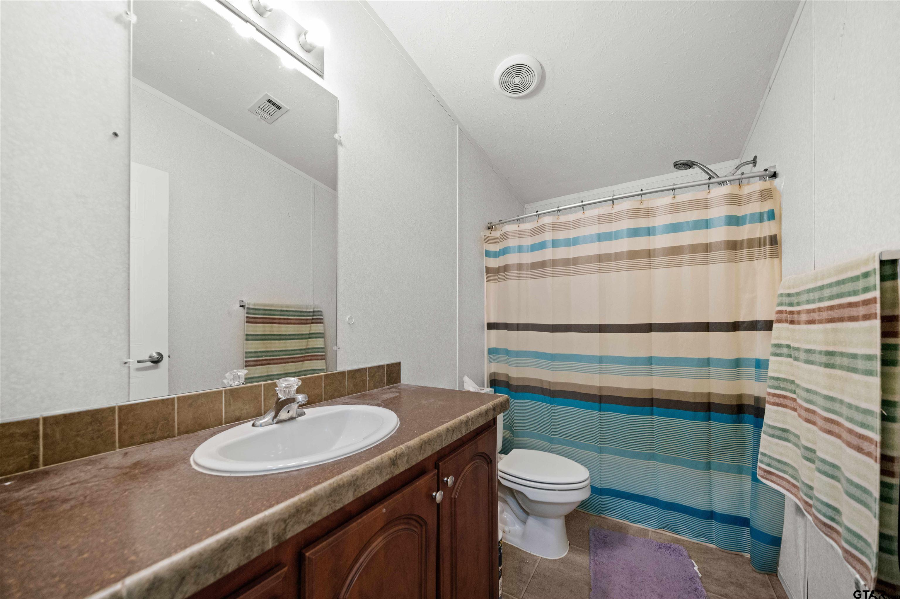 5611 Holiday Hills Road Tyler, TX 75708 - Photo 26 of 38 a bathroom with a granite countertop toilet sink and mirror